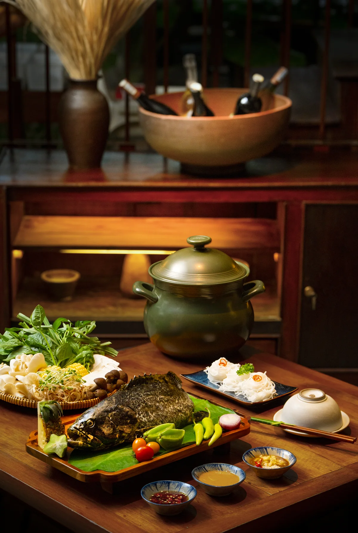 Fish hotpot setting with whole fish, garden vegetables, noodles and sauces at MiRi Hôm